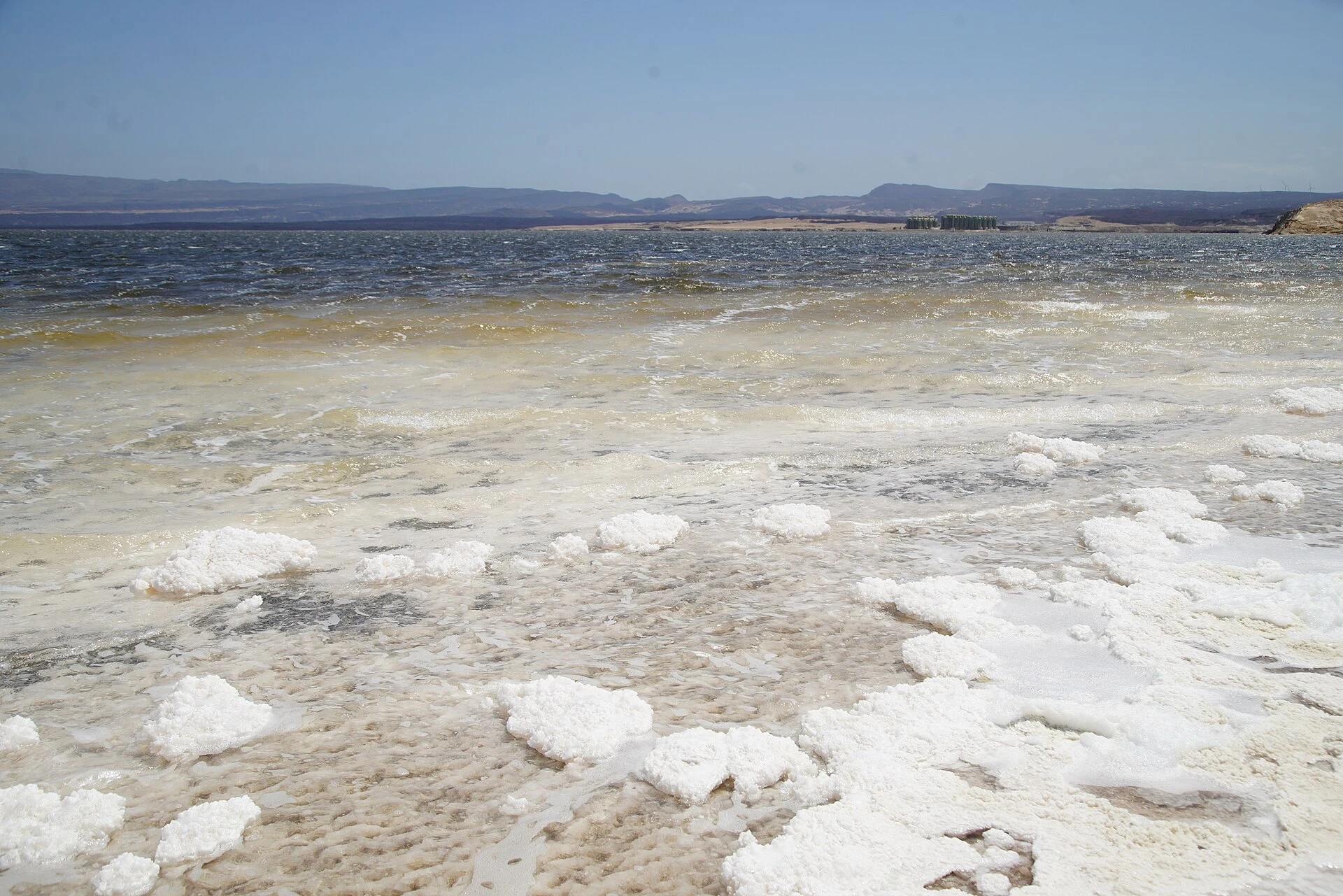 Wide view of Lake Assal with salt crusts, turquoise water, and volcanic ridges.