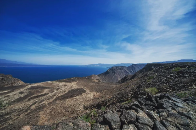 Panorama of Ghoubbet al-Kharab with dark volcanic coast and Devil's Island.
